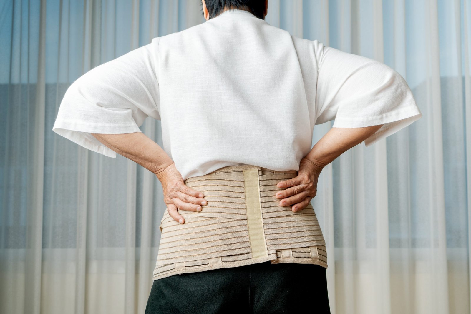 back pain senior woman wearing back support belt white background scaled
